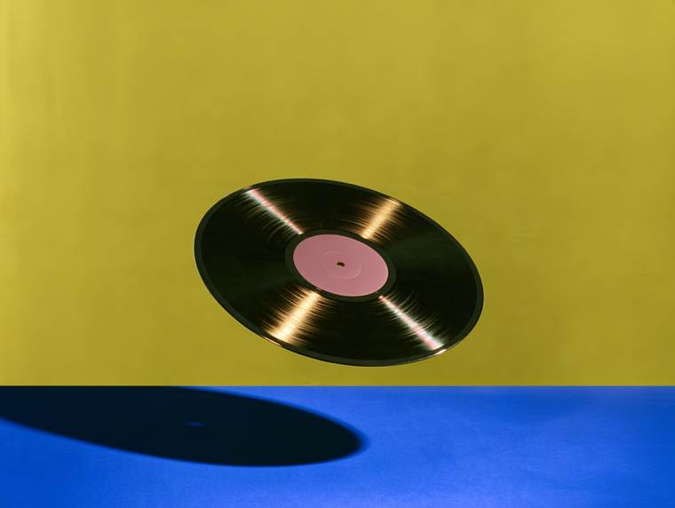 A vinyl record floating above a blue floor against an olive wall, casting a long shadow